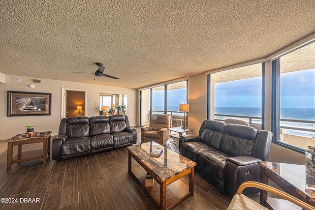 living room with a view of the beach, a water view, ceiling fan, a textured ceiling, and dark wood-type flooring