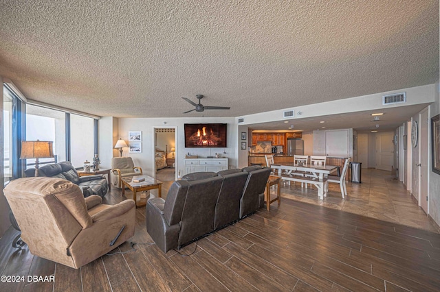 living room with a textured ceiling, a wall of windows, dark hardwood / wood-style flooring, and ceiling fan