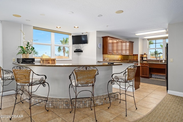 kitchen with kitchen peninsula, light tile patterned floors, sink, a breakfast bar area, and dark stone countertops