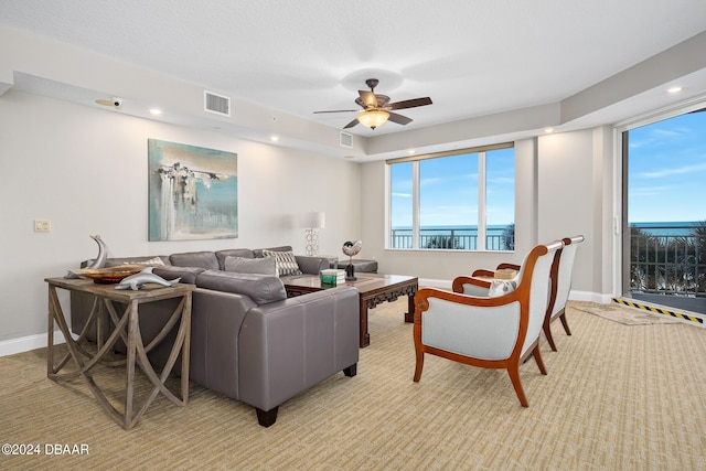 living room with a water view, a textured ceiling, and ceiling fan