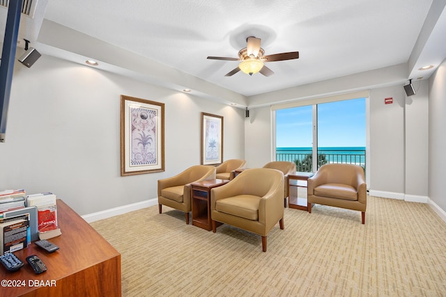 sitting room featuring a water view, light carpet, and ceiling fan