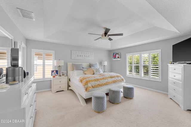 carpeted bedroom with multiple windows, ceiling fan, and a raised ceiling