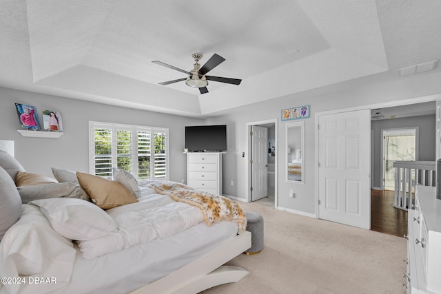 bedroom featuring light colored carpet, ceiling fan, a textured ceiling, and a tray ceiling