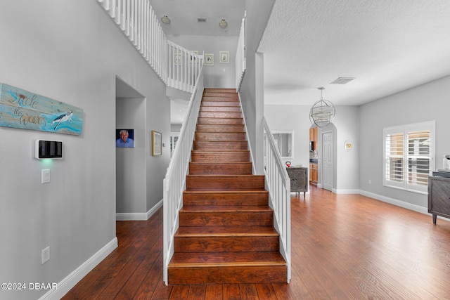 stairway featuring wood-type flooring, a notable chandelier, and a textured ceiling