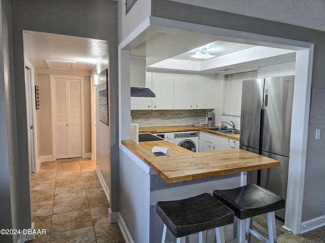 kitchen with stainless steel refrigerator, butcher block counters, a kitchen breakfast bar, washer / clothes dryer, and white cabinets