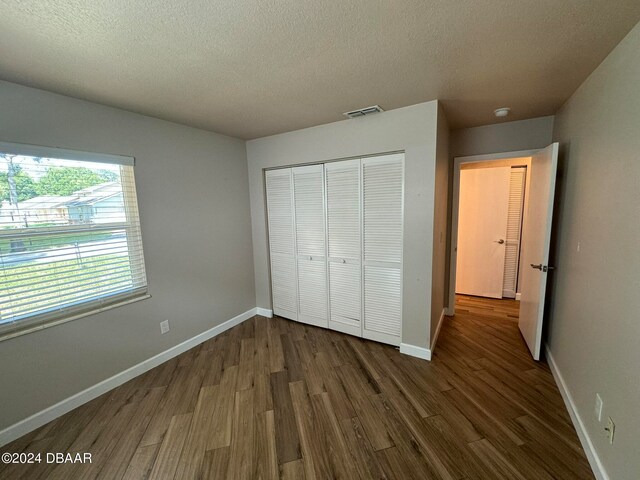 unfurnished bedroom featuring dark hardwood / wood-style flooring, a textured ceiling, and a closet