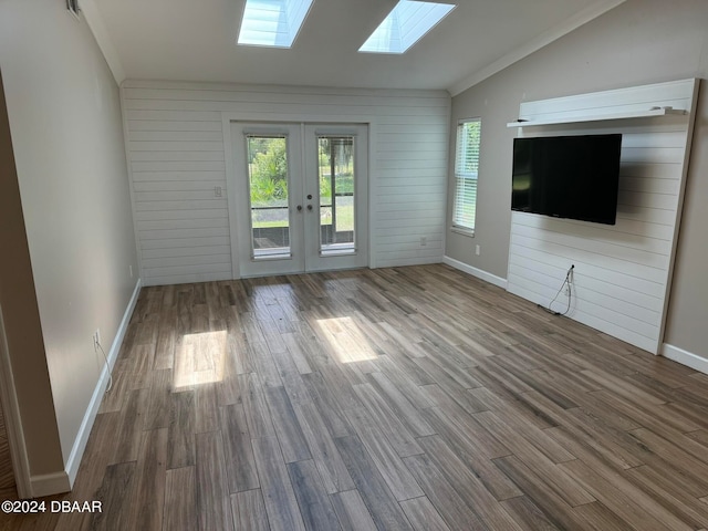 unfurnished living room featuring lofted ceiling with skylight, french doors, wood walls, and hardwood / wood-style flooring