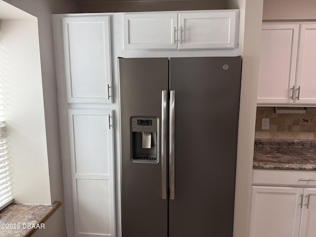 kitchen featuring white cabinets, stainless steel fridge, backsplash, and dark stone counters