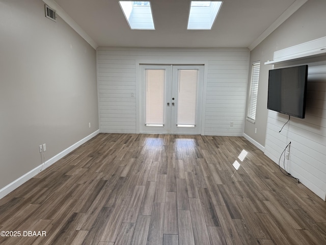 unfurnished living room featuring wood walls, crown molding, dark wood-type flooring, and french doors