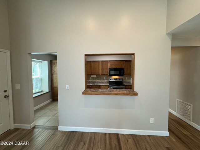 kitchen featuring stainless steel electric range, a towering ceiling, tasteful backsplash, kitchen peninsula, and light hardwood / wood-style flooring