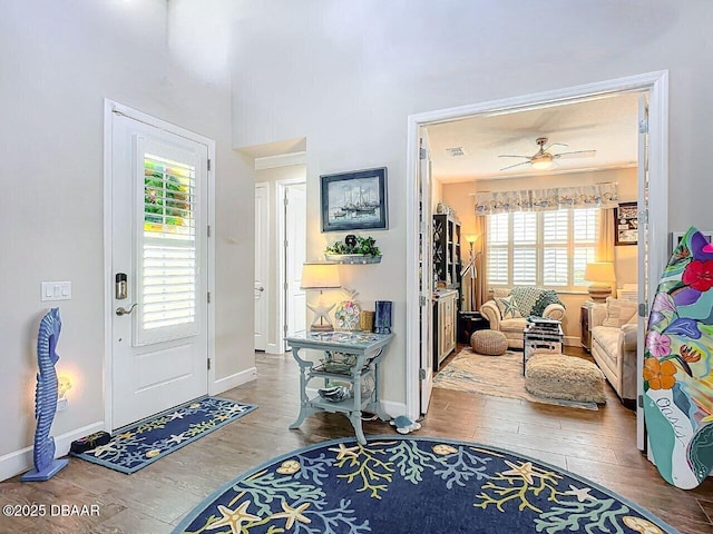 foyer with a ceiling fan, visible vents, baseboards, and wood finished floors