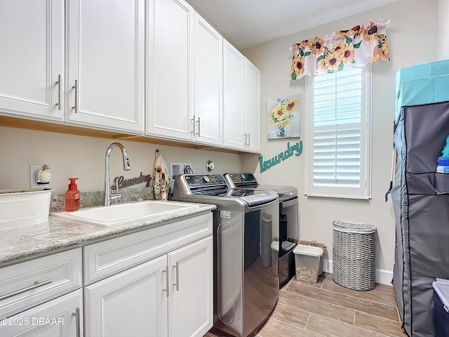 laundry room featuring cabinet space, wood tiled floor, a sink, washer and dryer, and baseboards