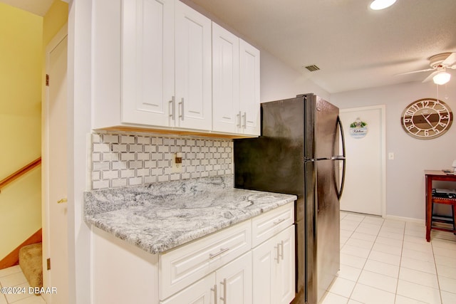 kitchen featuring black refrigerator, ceiling fan, white cabinetry, light tile patterned floors, and light stone countertops