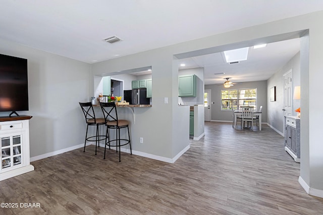 kitchen featuring a kitchen bar, black refrigerator, kitchen peninsula, green cabinets, and hardwood / wood-style flooring