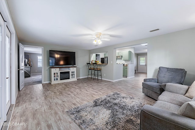 living room with ceiling fan, a fireplace, a healthy amount of sunlight, and light wood-type flooring