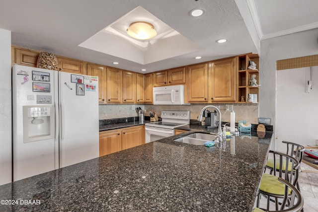 kitchen featuring sink, kitchen peninsula, dark stone counters, a tray ceiling, and white appliances