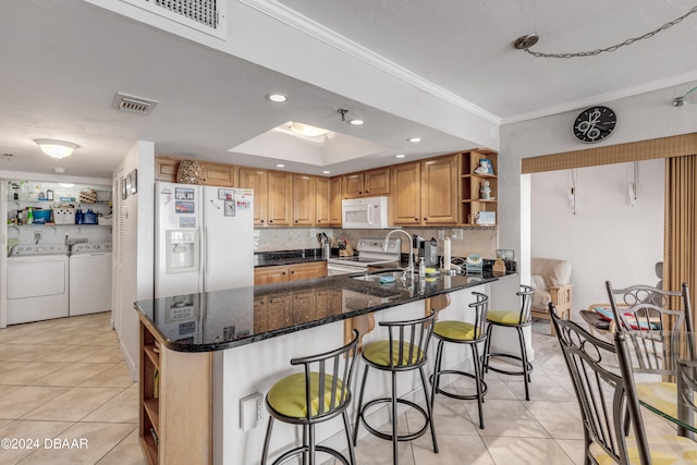 kitchen featuring sink, kitchen peninsula, ornamental molding, dark stone countertops, and white appliances