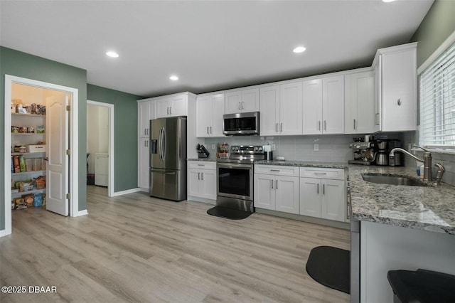 kitchen featuring light stone countertops, stainless steel appliances, sink, light hardwood / wood-style flooring, and white cabinets