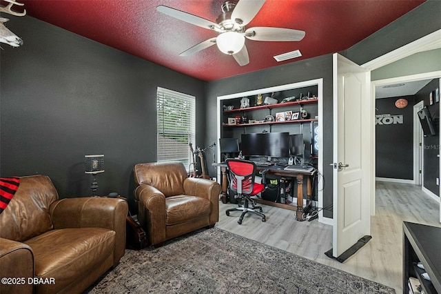 office space with built in shelves, ceiling fan, wood-type flooring, and a textured ceiling