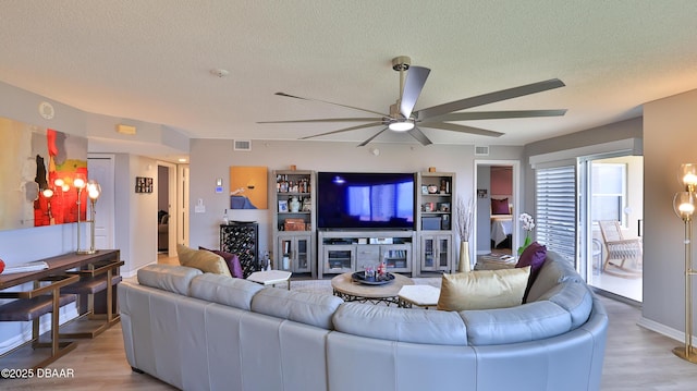 living room with ceiling fan, a textured ceiling, and light wood-type flooring