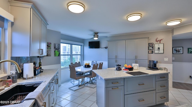 kitchen with sink, light tile patterned floors, gray cabinetry, a center island, and light stone counters