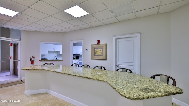 kitchen featuring light stone counters, a paneled ceiling, sink, and white cabinets