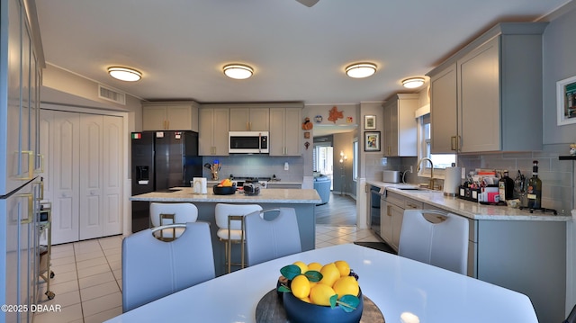 kitchen with sink, light tile patterned floors, gray cabinetry, backsplash, and a center island