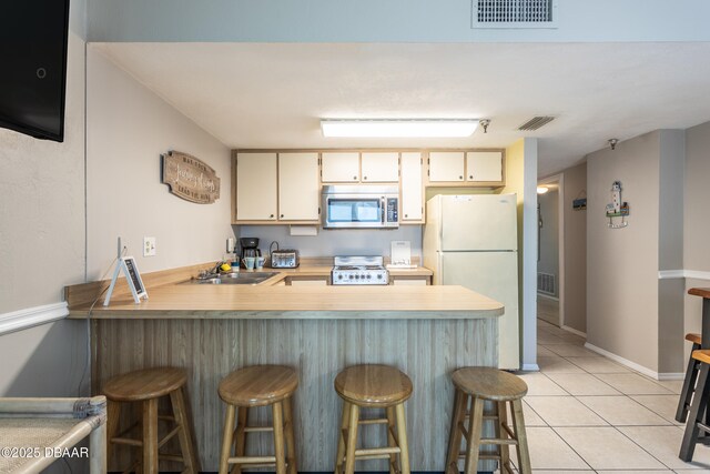 kitchen featuring white refrigerator, stove, a breakfast bar, and kitchen peninsula