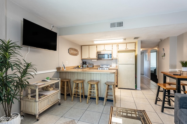 kitchen with light tile patterned floors, a kitchen breakfast bar, kitchen peninsula, white fridge, and cream cabinetry