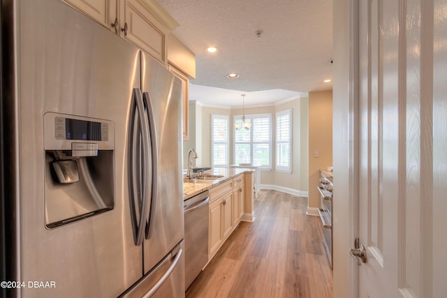 kitchen featuring light hardwood / wood-style floors, stainless steel appliances, hanging light fixtures, sink, and light stone countertops