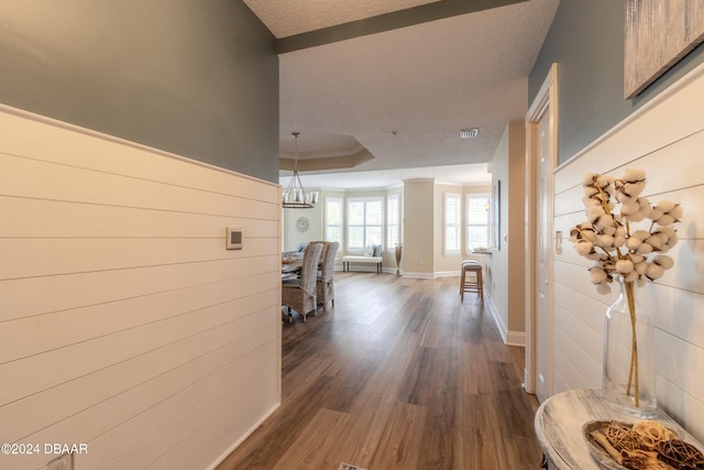 hall featuring dark hardwood / wood-style floors, a textured ceiling, a raised ceiling, and a notable chandelier