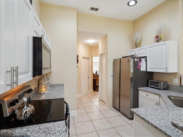 kitchen featuring light tile patterned flooring, light stone countertops, white cabinetry, and appliances with stainless steel finishes