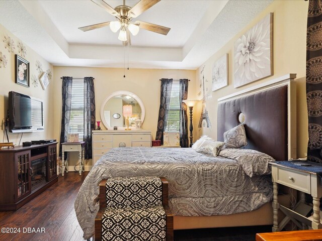 bedroom with dark hardwood / wood-style flooring, a raised ceiling, multiple windows, and ceiling fan