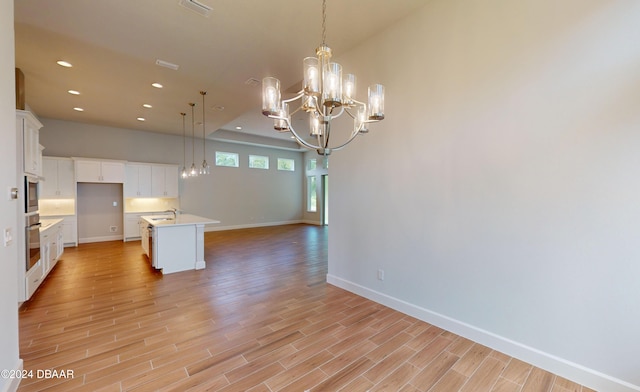 kitchen with decorative light fixtures, light hardwood / wood-style flooring, a kitchen island with sink, and white cabinetry