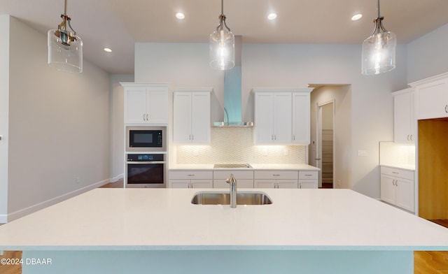 kitchen featuring black microwave, a kitchen island with sink, sink, decorative light fixtures, and oven