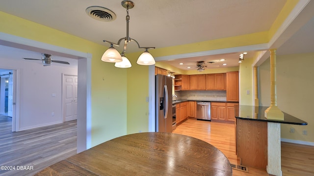 kitchen with tasteful backsplash, kitchen peninsula, pendant lighting, ceiling fan with notable chandelier, and appliances with stainless steel finishes