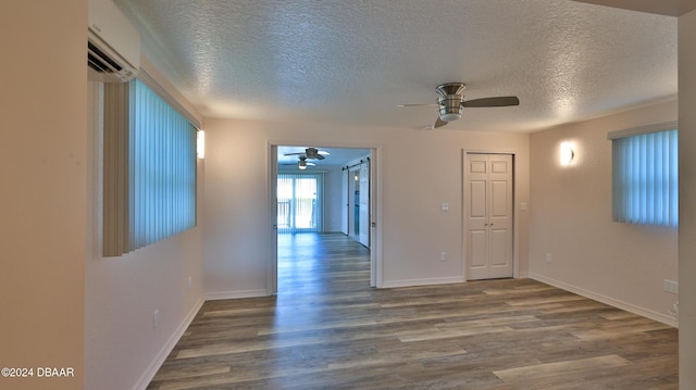 empty room with hardwood / wood-style flooring, ceiling fan, an AC wall unit, and a textured ceiling