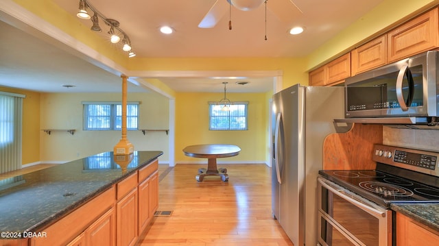 kitchen with dark stone countertops, light hardwood / wood-style floors, hanging light fixtures, and appliances with stainless steel finishes