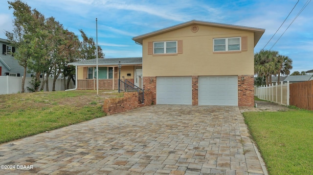 split level home with covered porch, a garage, and a front lawn