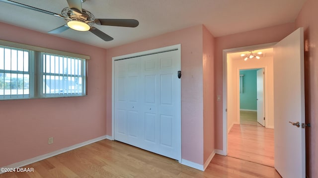 unfurnished bedroom with ceiling fan with notable chandelier, light hardwood / wood-style floors, and a closet