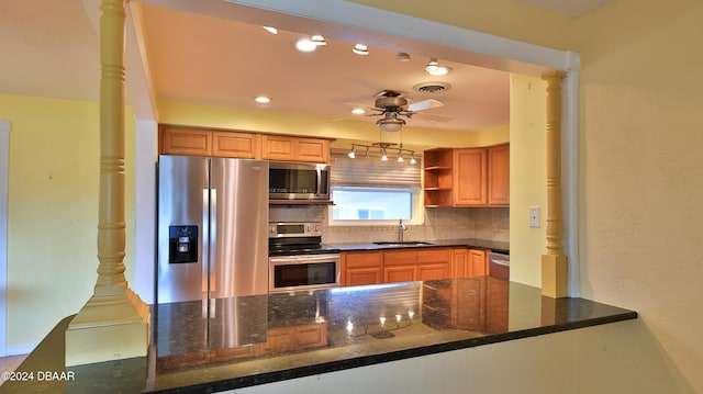 kitchen featuring kitchen peninsula, decorative columns, stainless steel appliances, sink, and dark stone countertops