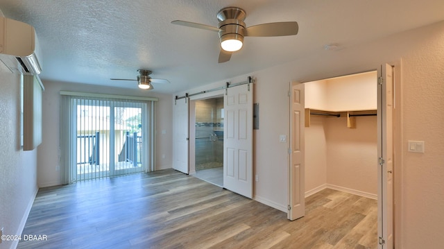 unfurnished bedroom featuring a walk in closet, ceiling fan, a barn door, light hardwood / wood-style flooring, and a closet