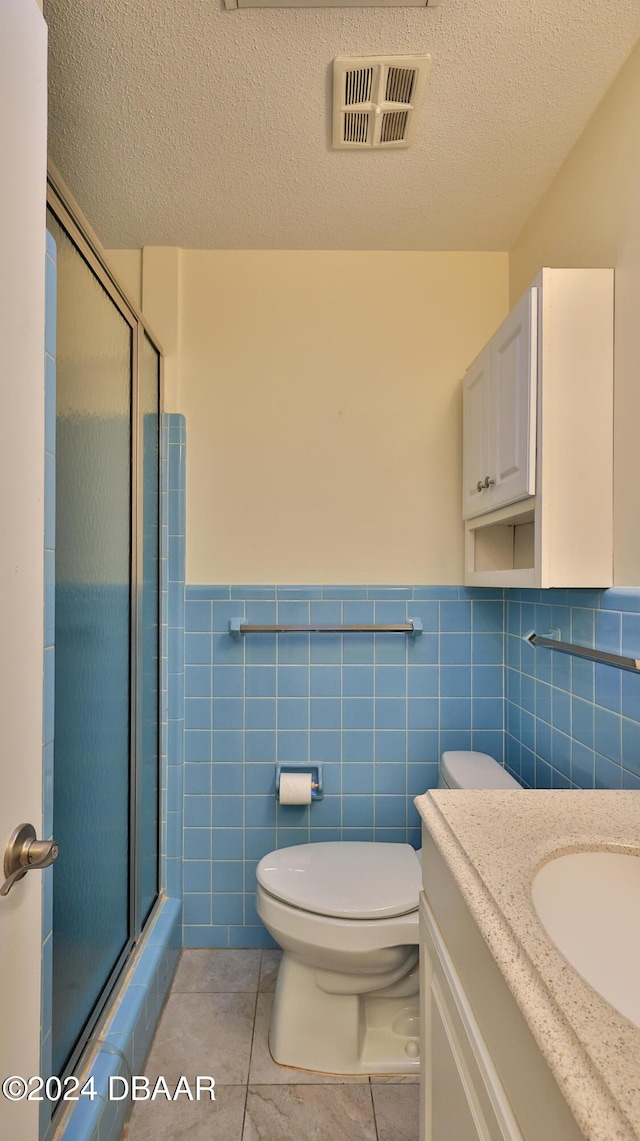 bathroom featuring a textured ceiling, a shower with door, toilet, and tile walls