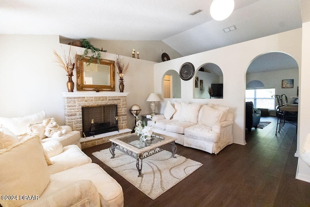 living room featuring dark hardwood / wood-style flooring, a stone fireplace, and vaulted ceiling