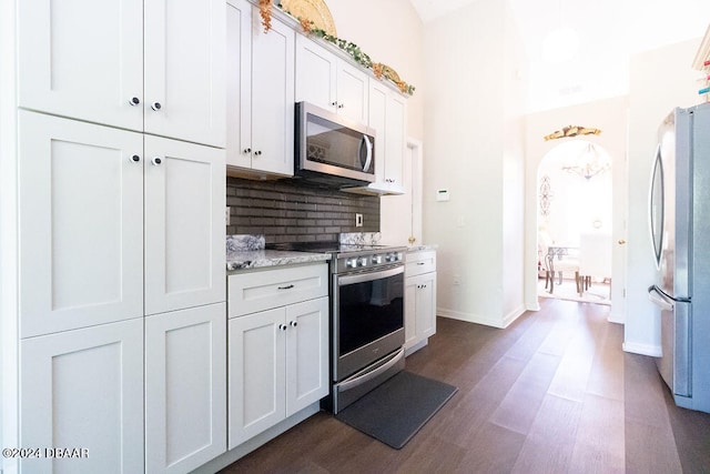 kitchen with dark hardwood / wood-style flooring, white cabinets, decorative backsplash, light stone countertops, and appliances with stainless steel finishes