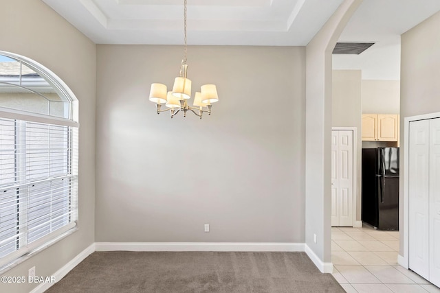 carpeted spare room featuring a notable chandelier and a tray ceiling