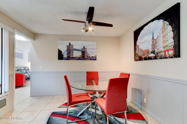 tiled dining area with a wainscoted wall, a ceiling fan, and a textured ceiling