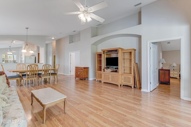 living area featuring visible vents, baseboards, ceiling fan with notable chandelier, light wood-style floors, and high vaulted ceiling