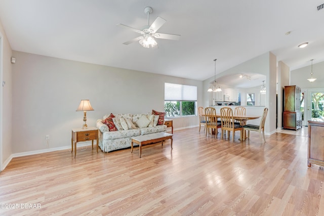 living room with visible vents, ceiling fan with notable chandelier, light wood-style floors, baseboards, and vaulted ceiling