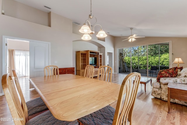 dining room with ceiling fan with notable chandelier, light wood-style floors, visible vents, and high vaulted ceiling